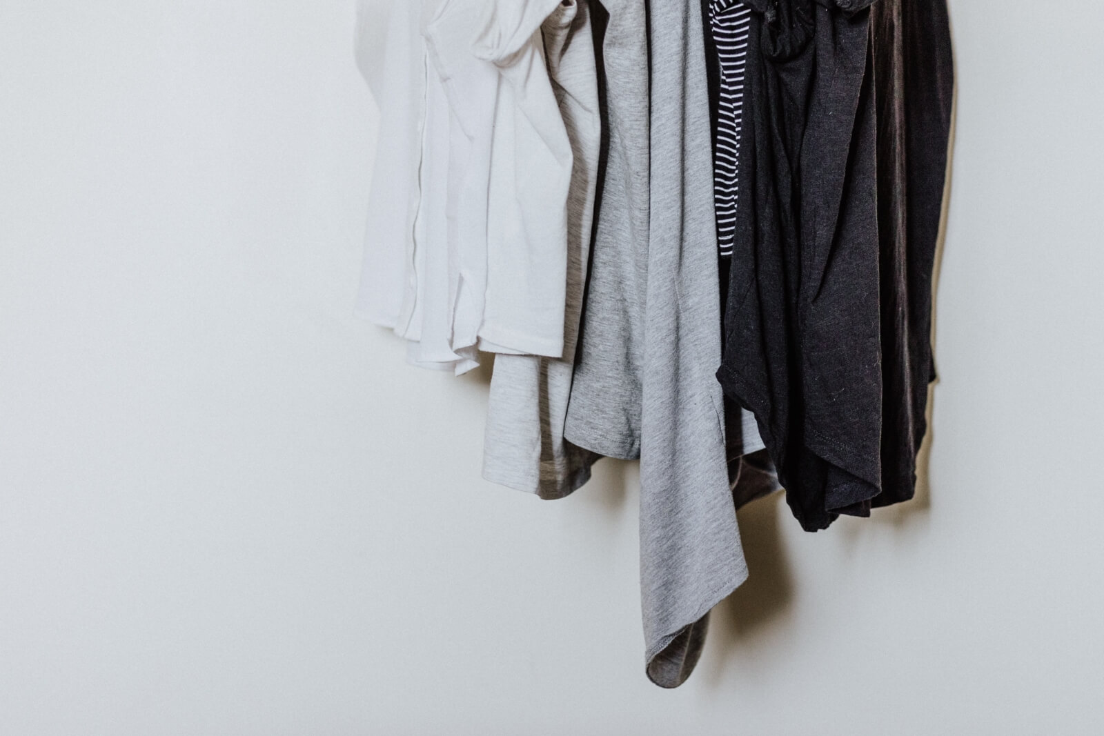 Grey, white and black shirts hang on a clothing rack.