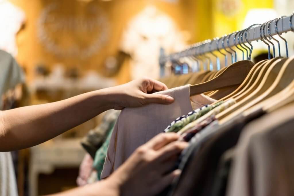 A closeup of a woman sorting through clothing racks at a store.